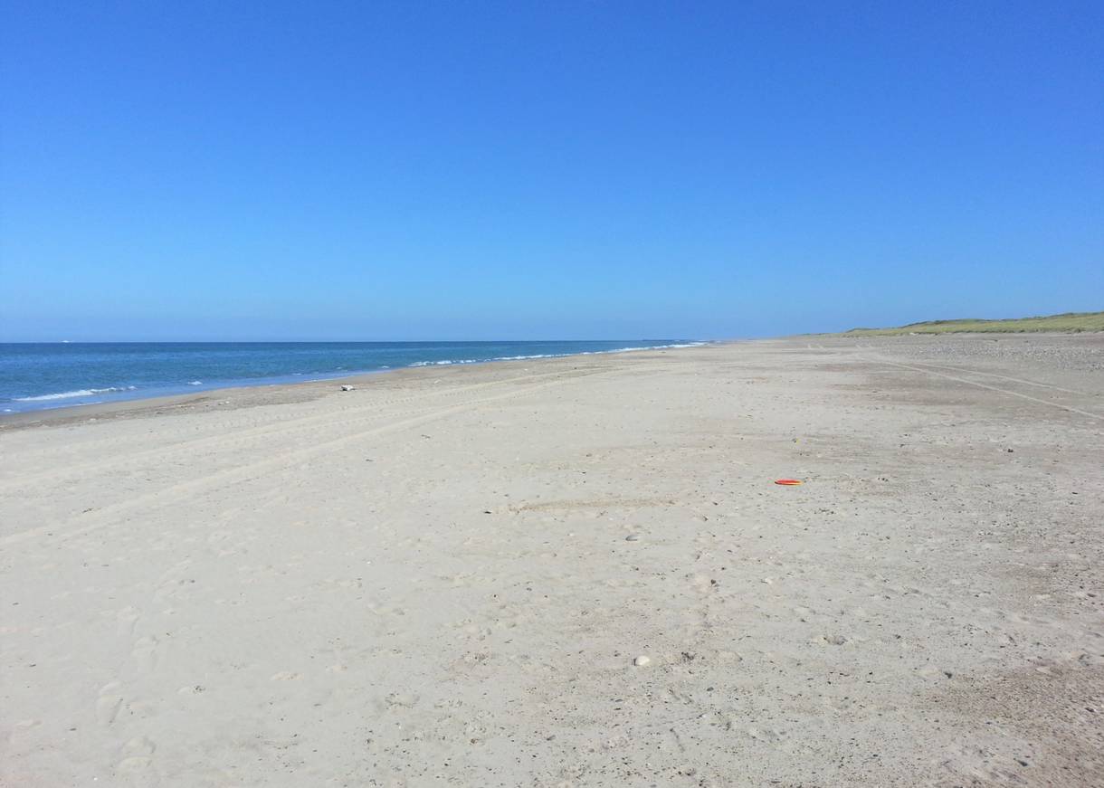 Sehr breiter, menschenleerer Strand unter blauem Himmel