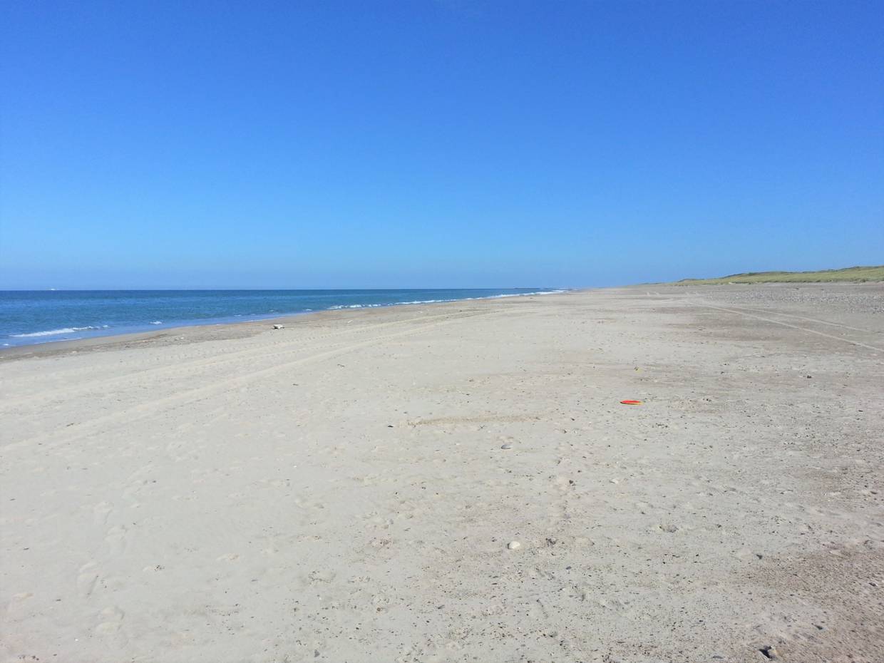 Sehr breiter, menschenleerer Strand unter blauem Himmel