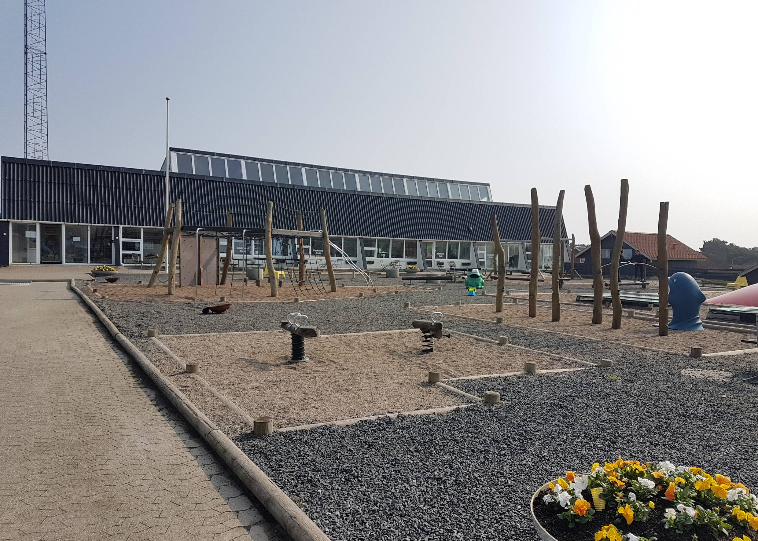 Spielplatz, dahinter ein langes Gebäude mit schwarzem Dach