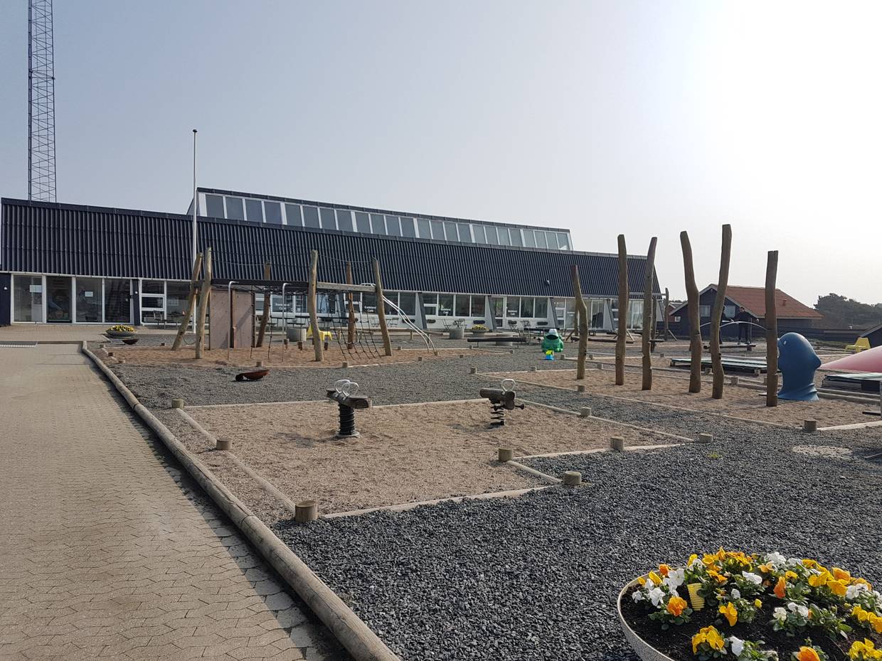 Spielplatz, dahinter ein langes Gebäude mit schwarzem Dach
