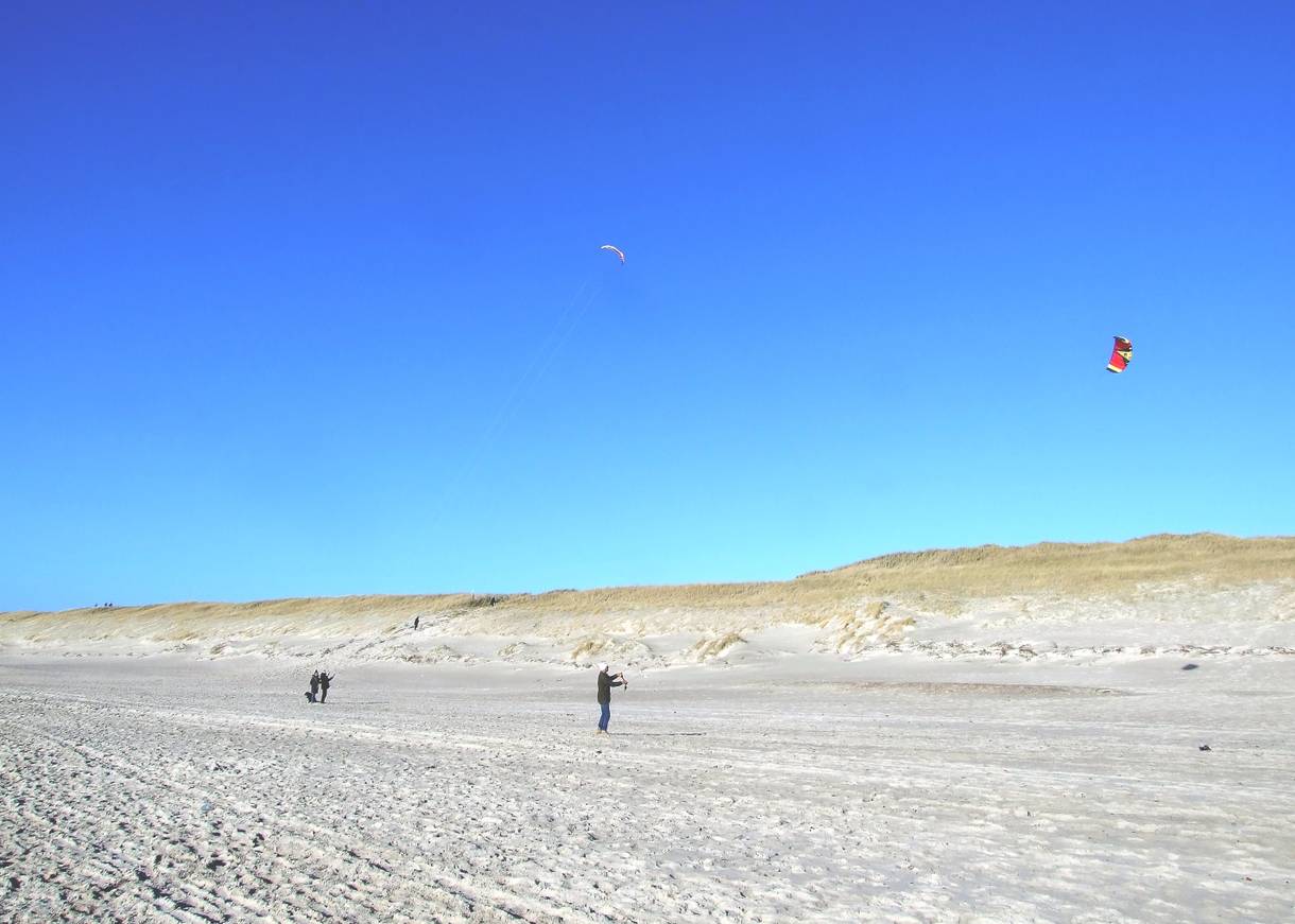 Nordseestrand und Dünen, drei Personen lassen einen Drachen fliegen