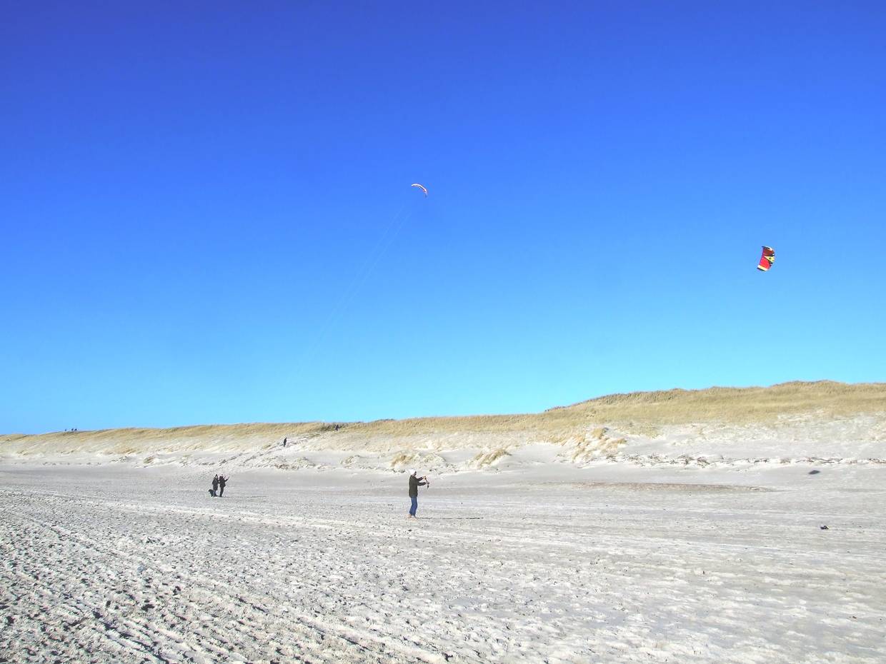 Zwei Menschen auf einem breiten Sandstrand im Winter, die einen Drachen steigen lassen