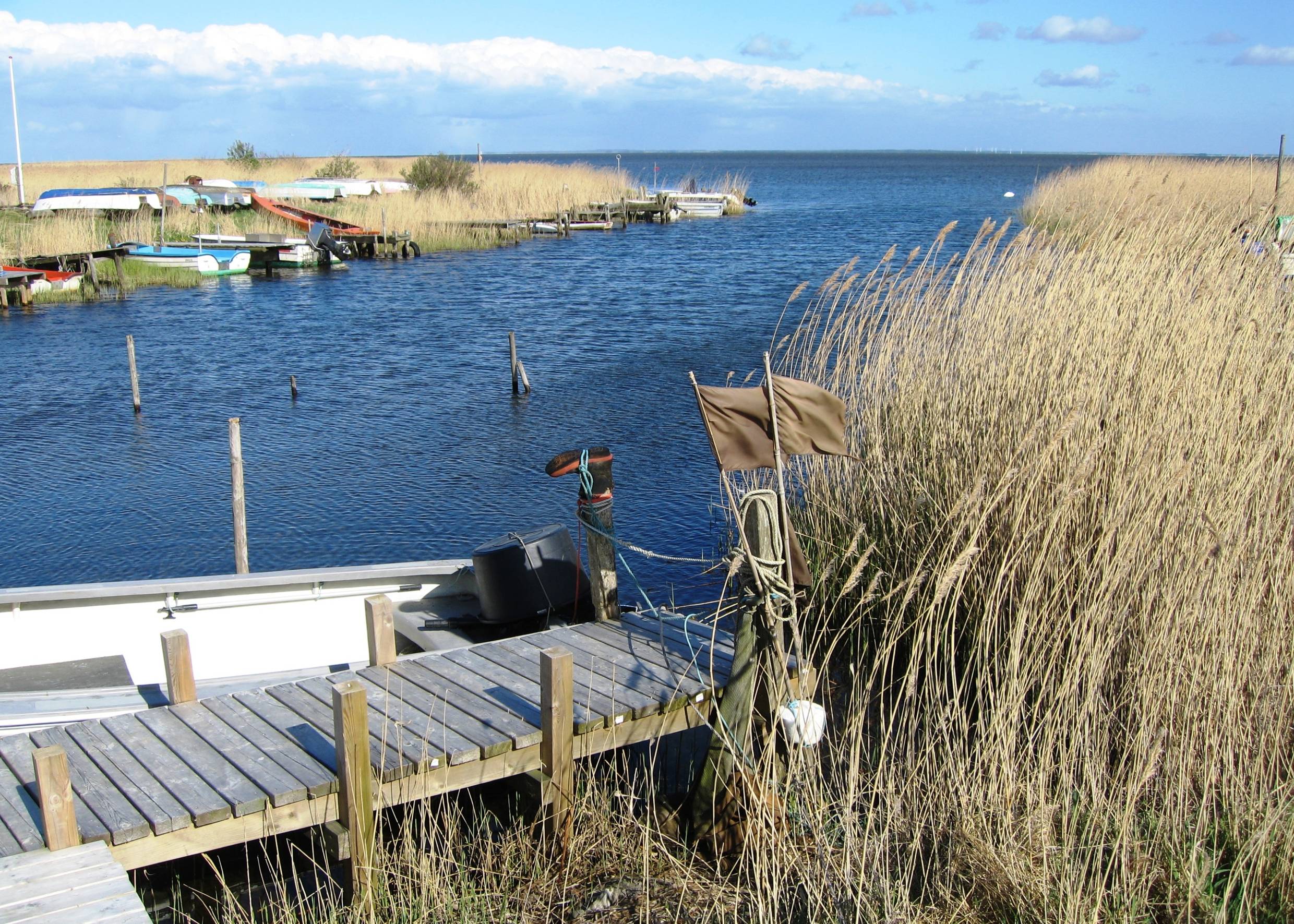 Holzsteg am Fjord, dahinter ein weißes Boot und Angelzubehör