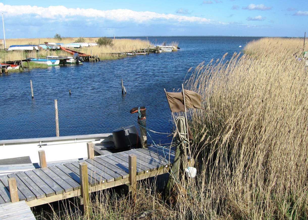 Holzsteg am Fjord, dahinter ein weißes Boot und Angelzubehör