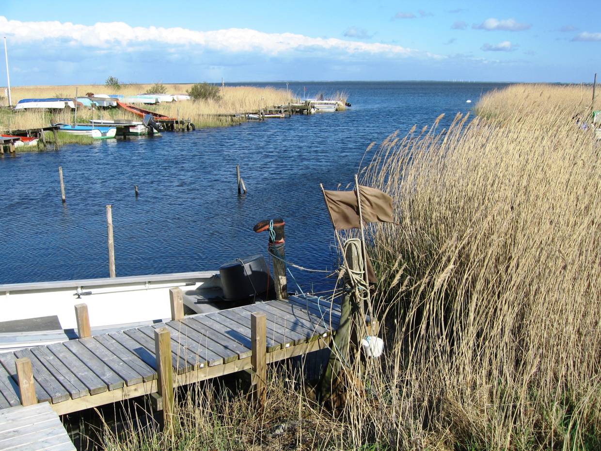 Holzsteg am Fjord, dahinter ein weißes Boot und Angelzubehör
