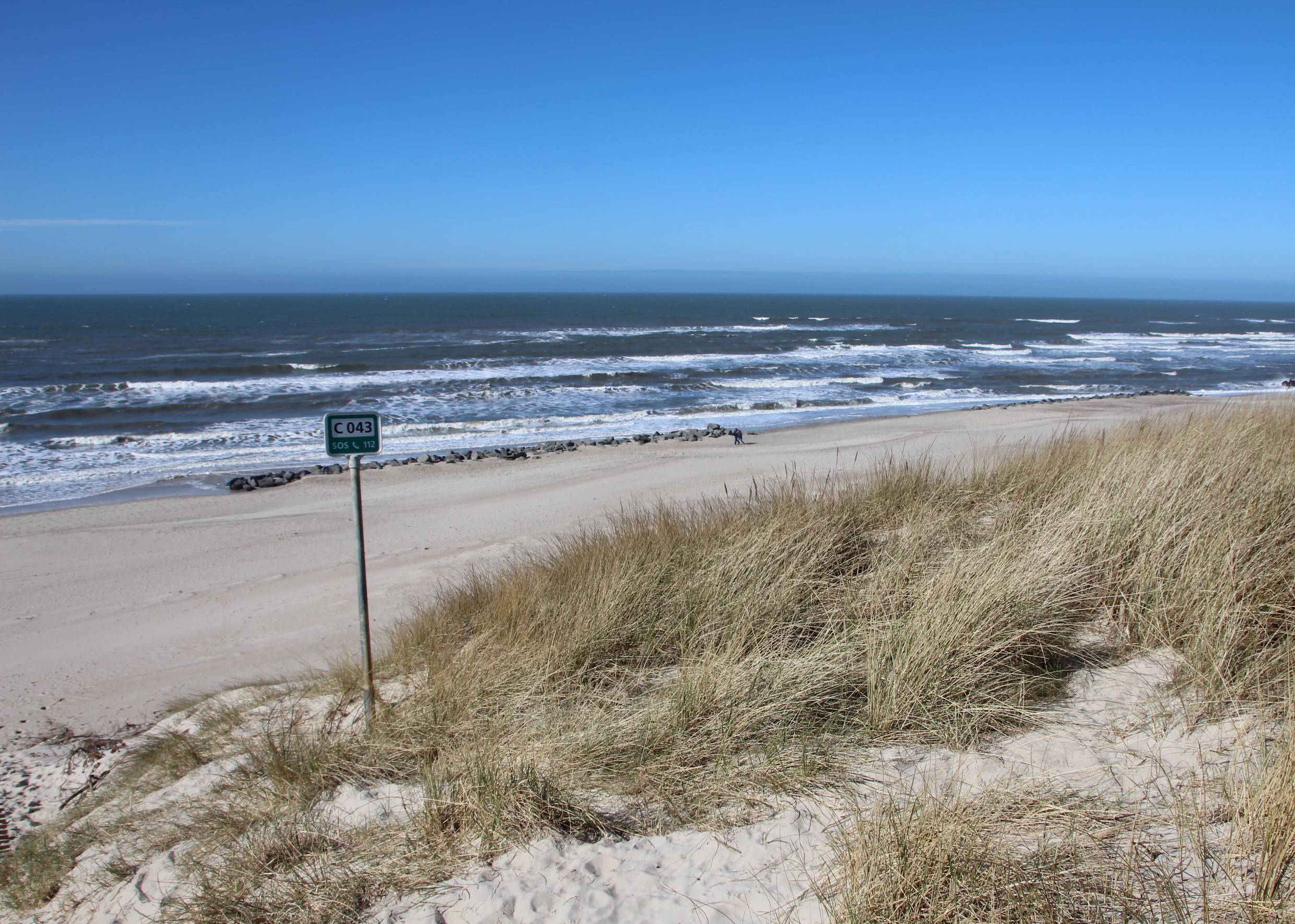 Blick von der Düne zur Nordsee, im Bild ein Schild mit Srrandnummer und Granitblöcke am Wasser