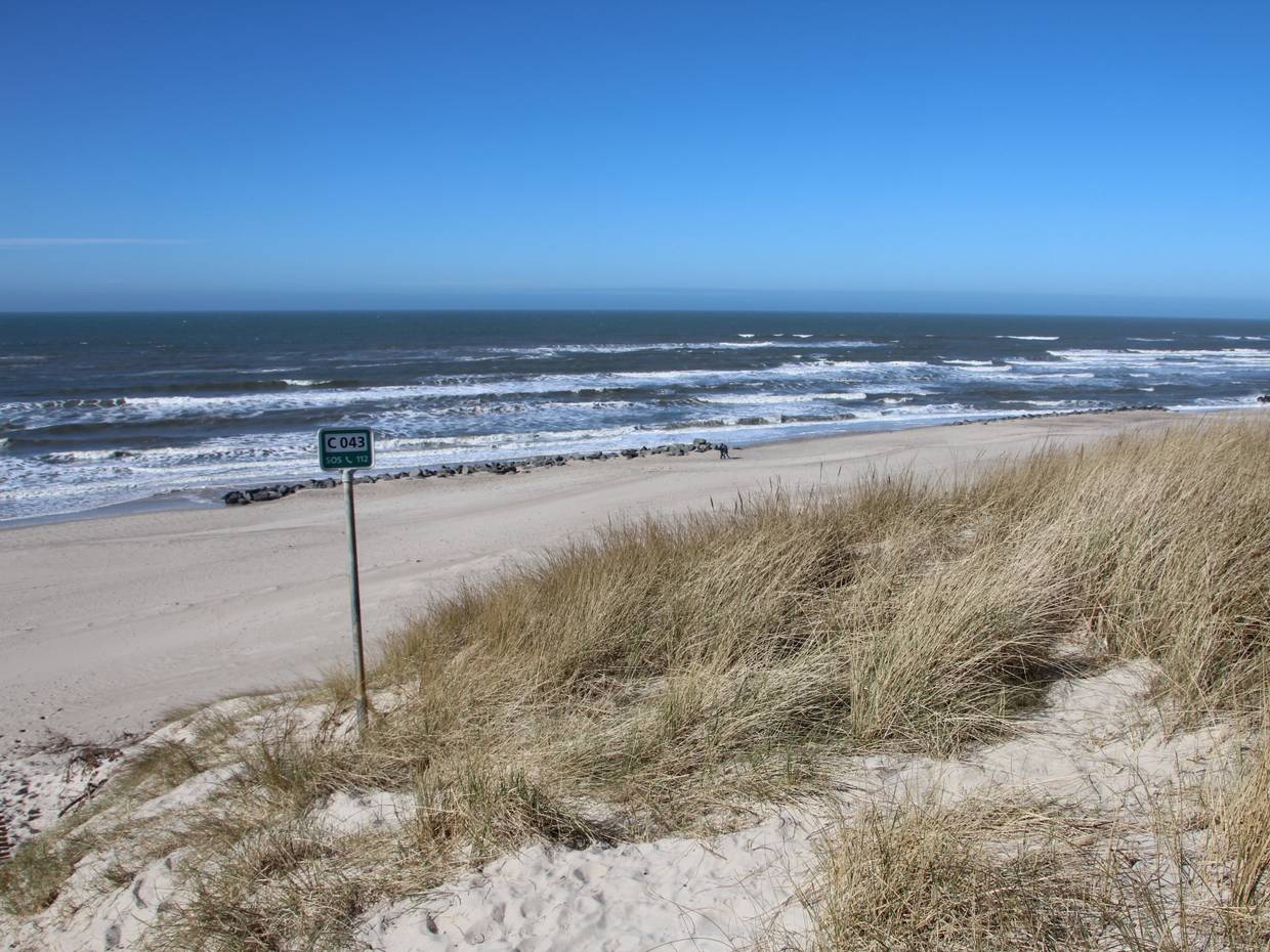 Blick von der Düne zur Nordsee, im Bild ein Schild mit Srrandnummer und Granitblöcke am Wasser