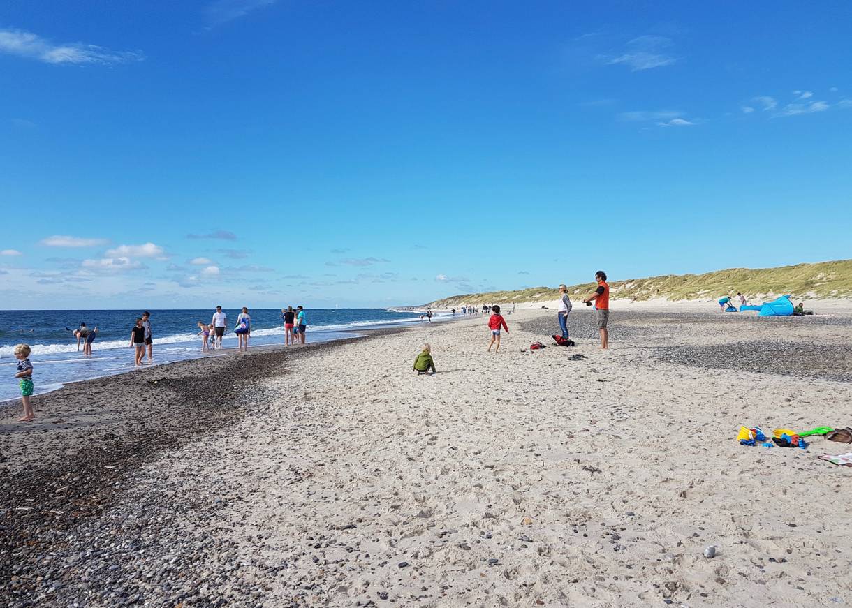 Breiter Sandstrand mit Badegästen unter blauem Himmel an der Nordsee