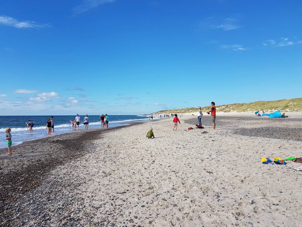 Breiter Sandstrand mit Badegästen unter blauem Himmel an der Nordsee