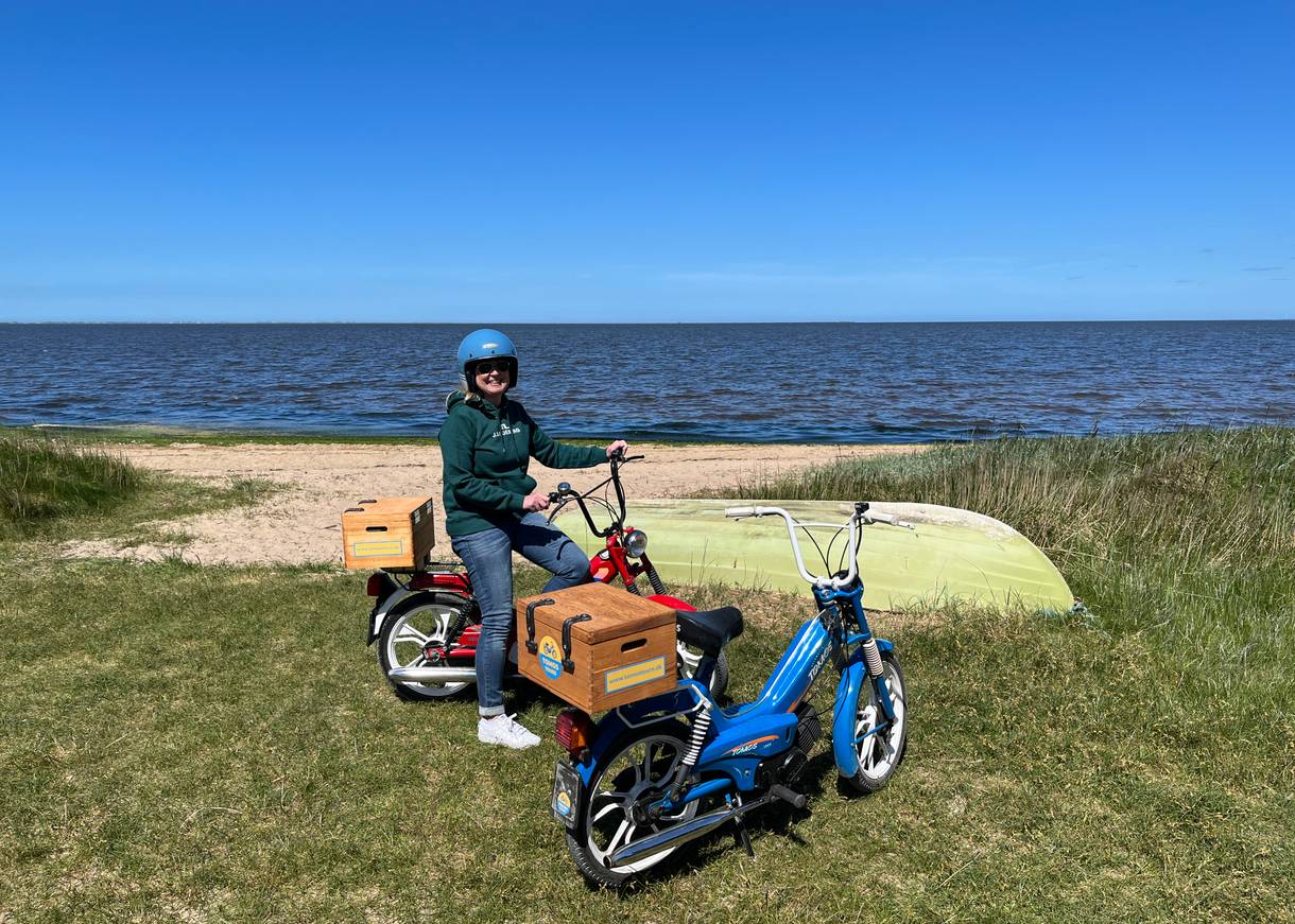 Zwei Mopeds am Fjordstrand, auf einem Sitzt eine Frau mit Helm