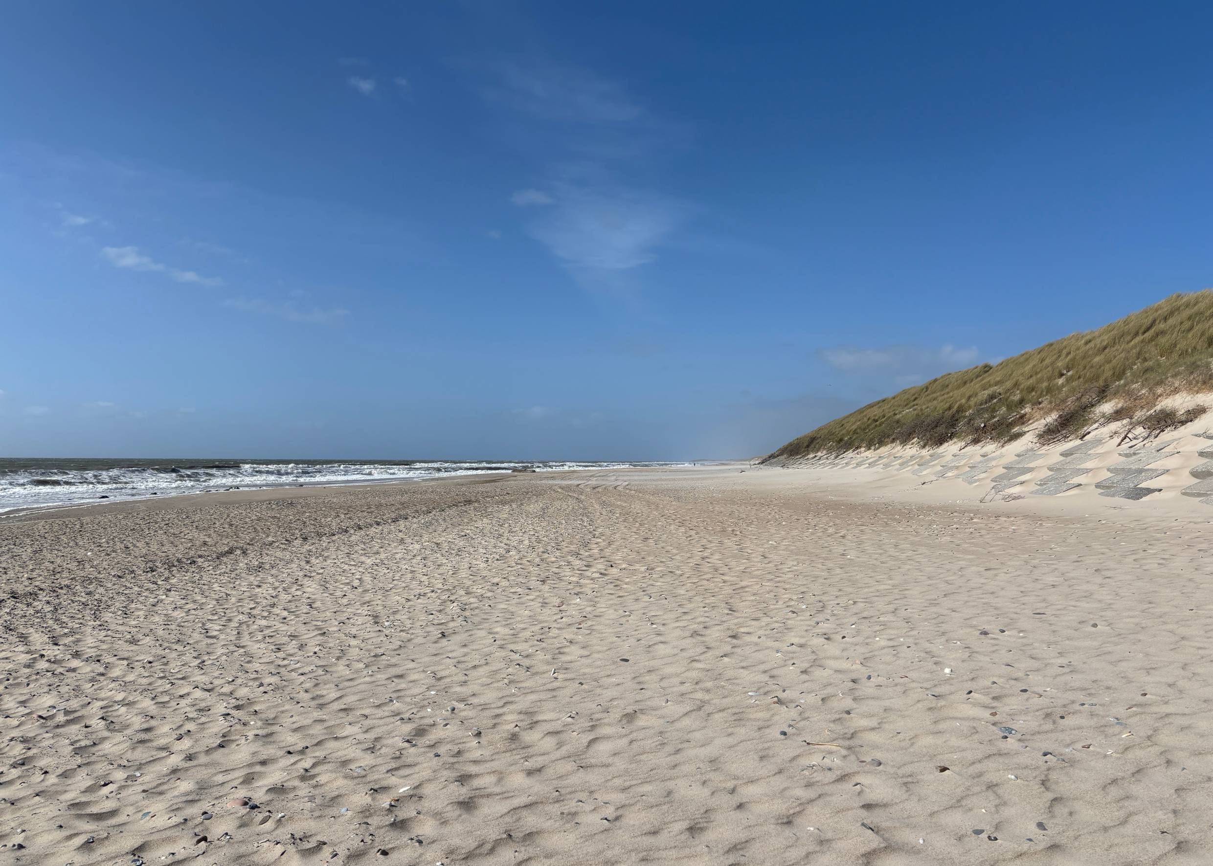 Sandstrand vor grüenen Dünen bei Sonne