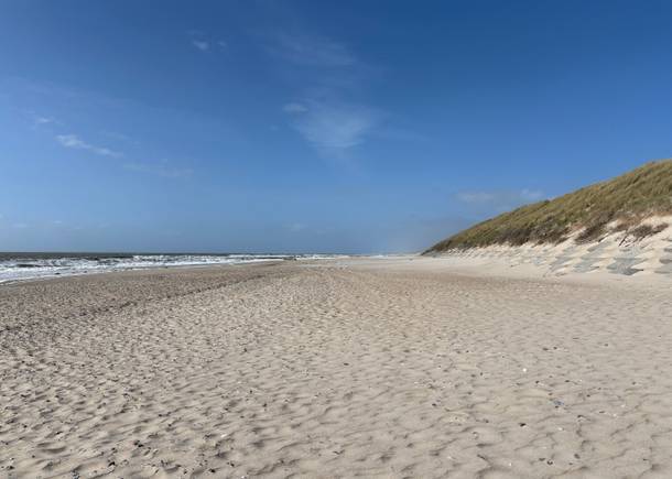 Sandstrand vor grüenen Dünen bei Sonne