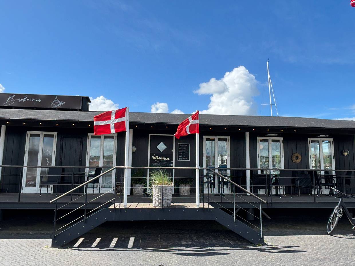 Ein Restaurant in einem schwarzen Holzgebäude mit zwei Fahnenmasten davor und Sitzplätze
