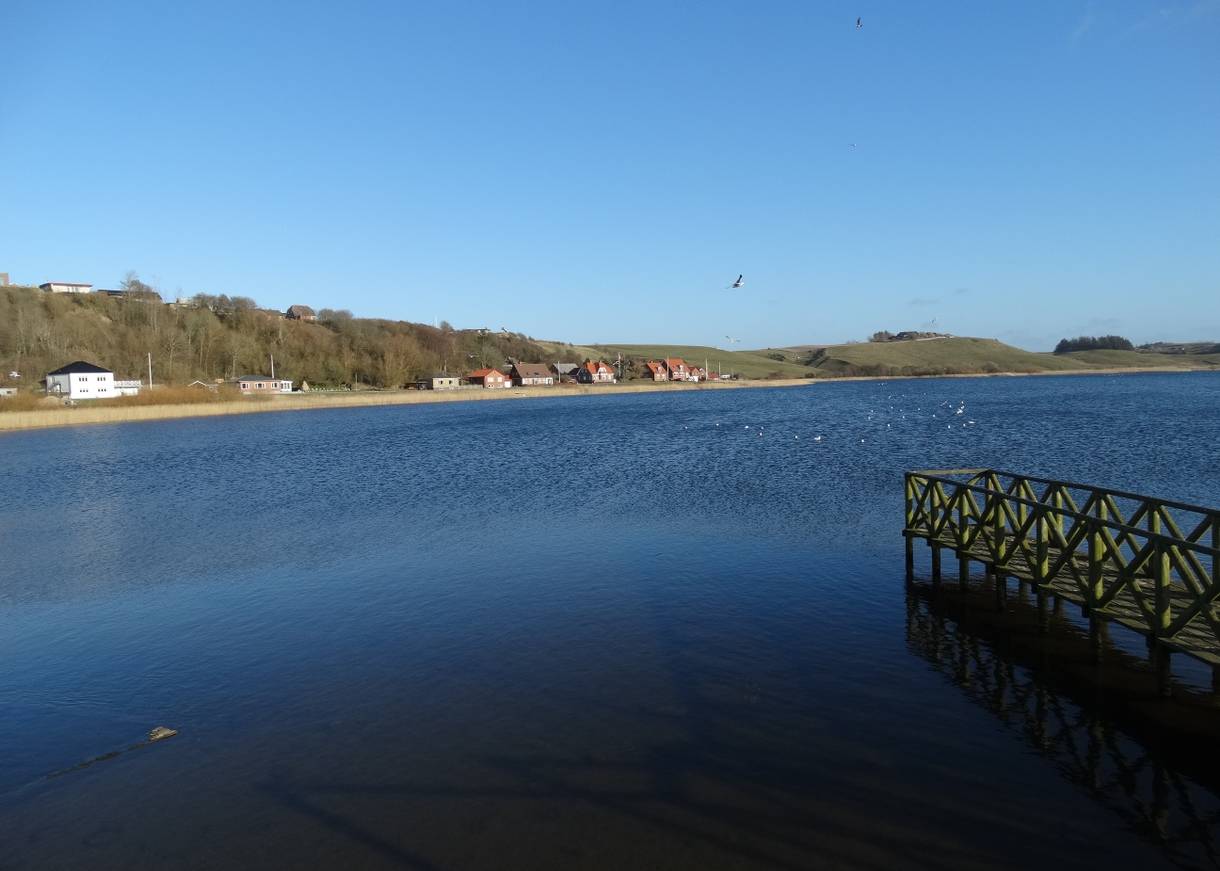Blauer, windstiller See mit einem Steg im Vordergrund