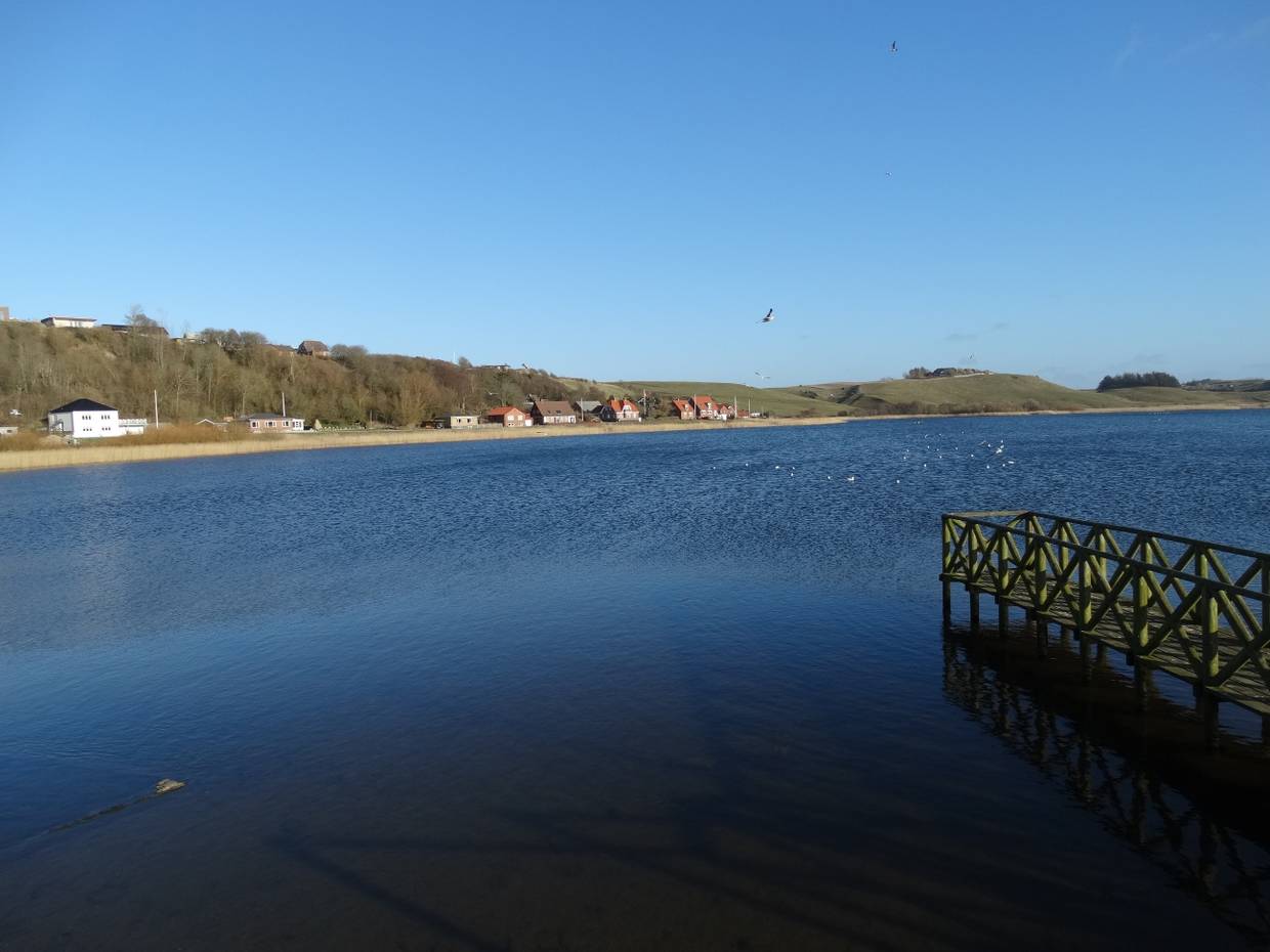 Blauer, windstiller See mit einem Steg im Vordergrund