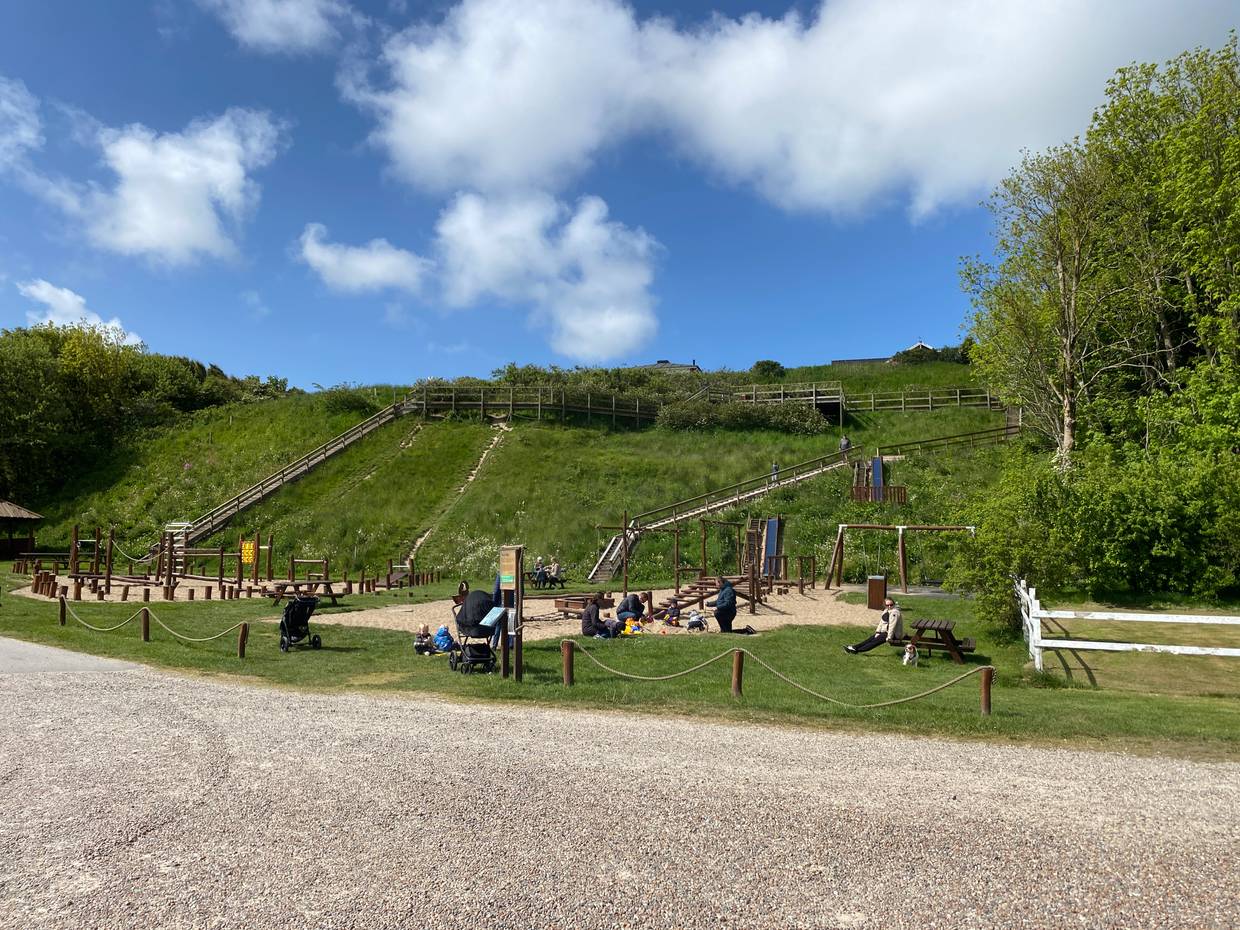 Spielplatz vor einem grünen Hügel bei Sommerwetter