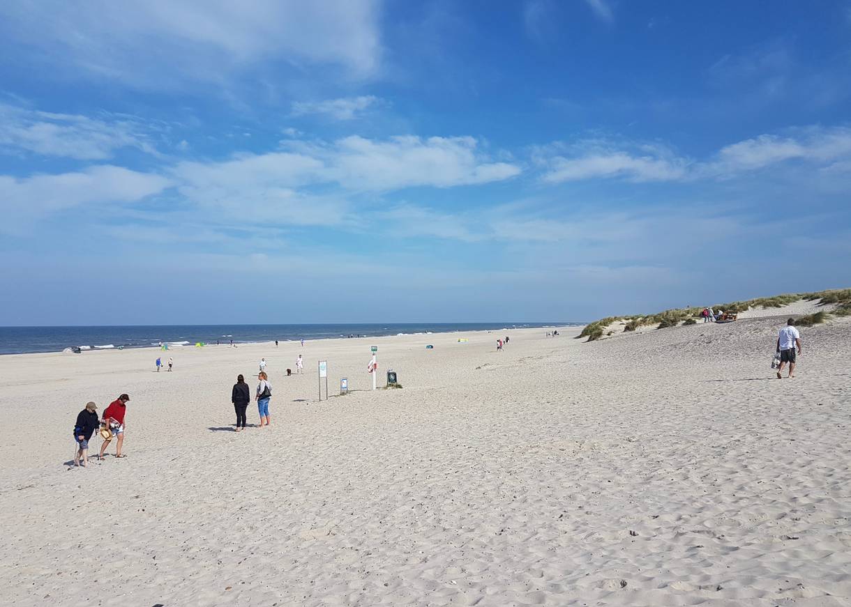 Breiter Sandstrand mit vielen Badegästen und Dünen im Hintergrund