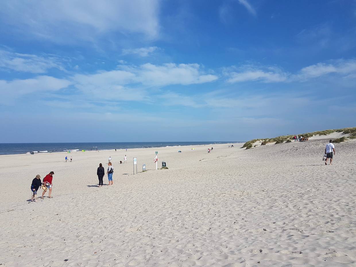 Breiter Sandstrand mit vielen Badegästen und Dünen im Hintergrund