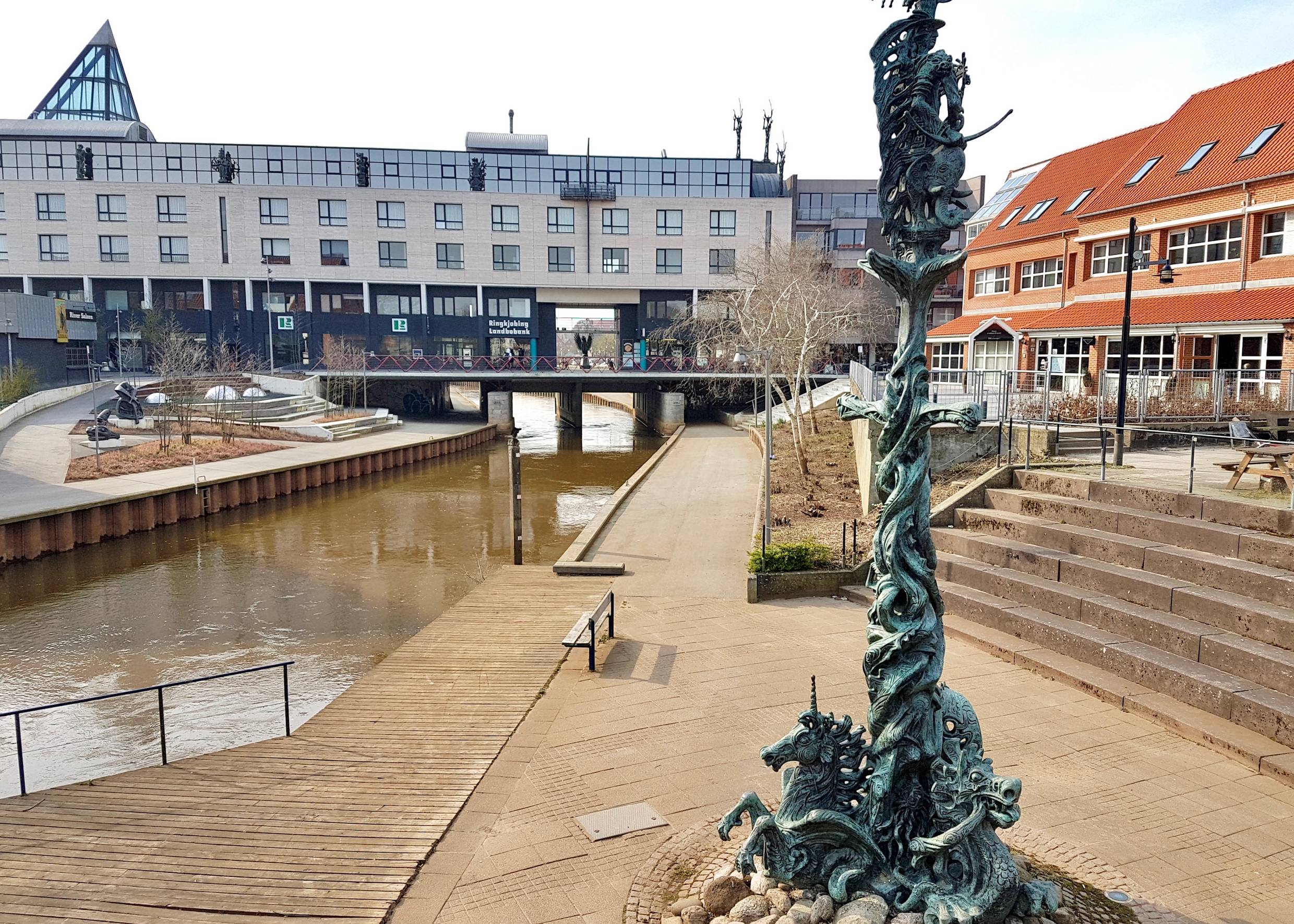 Befestigter Bachlauf, dahinter ein großes Bankgegebäude mit Skulpturen auf dem Dach