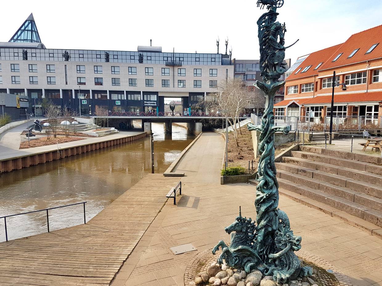 Befestigter Bachlauf, dahinter ein großes Bankgegebäude mit Skulpturen auf dem Dach