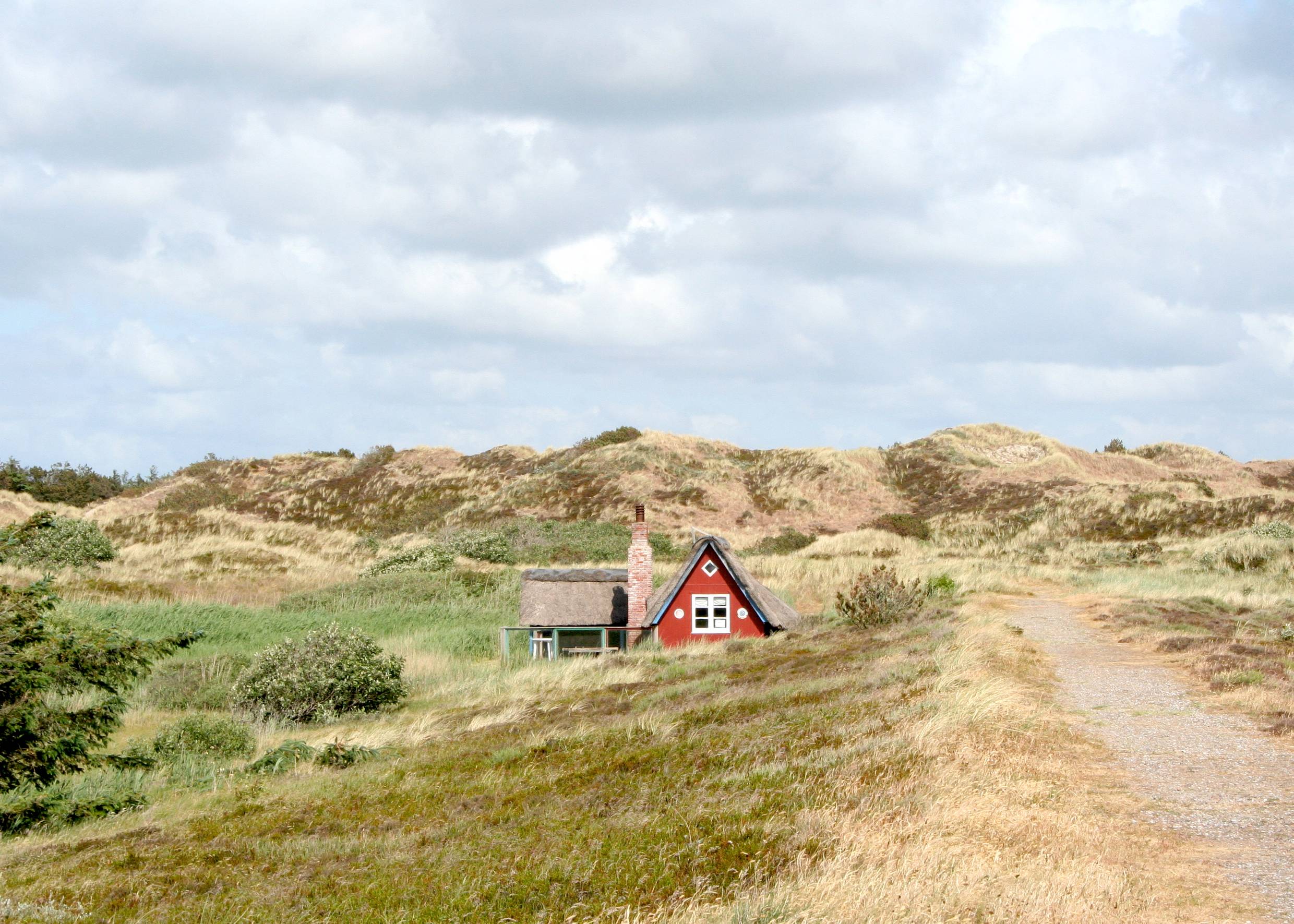 Wanderweg durch die Dünenlandschaft mit einem roten Reetdachhaus am Weg