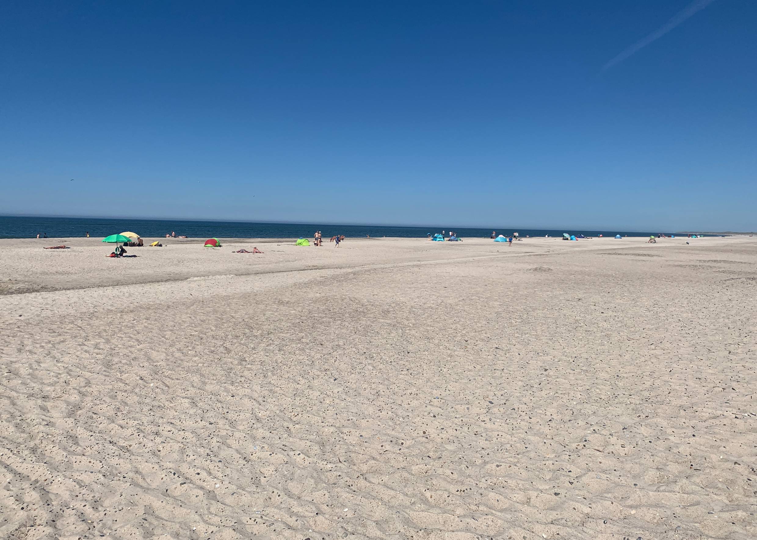 Blick auf einen breiten, weißen Sandstrand mit Sommergästen