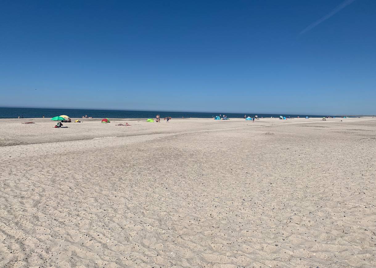 Blick auf einen breiten, weißen Sandstrand mit Sommergästen