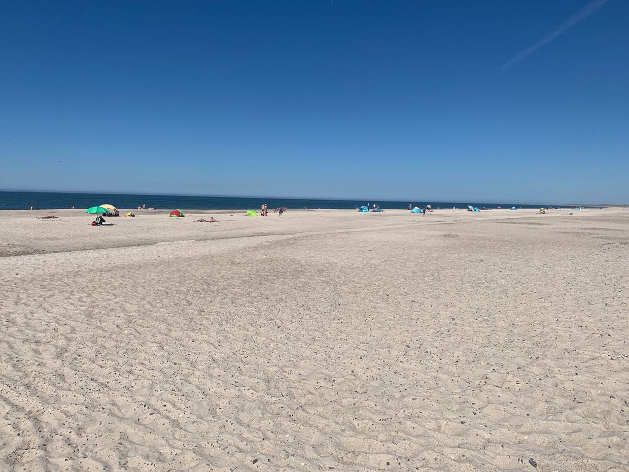 Blick auf einen breiten, weißen Sandstrand mit Sommergästen