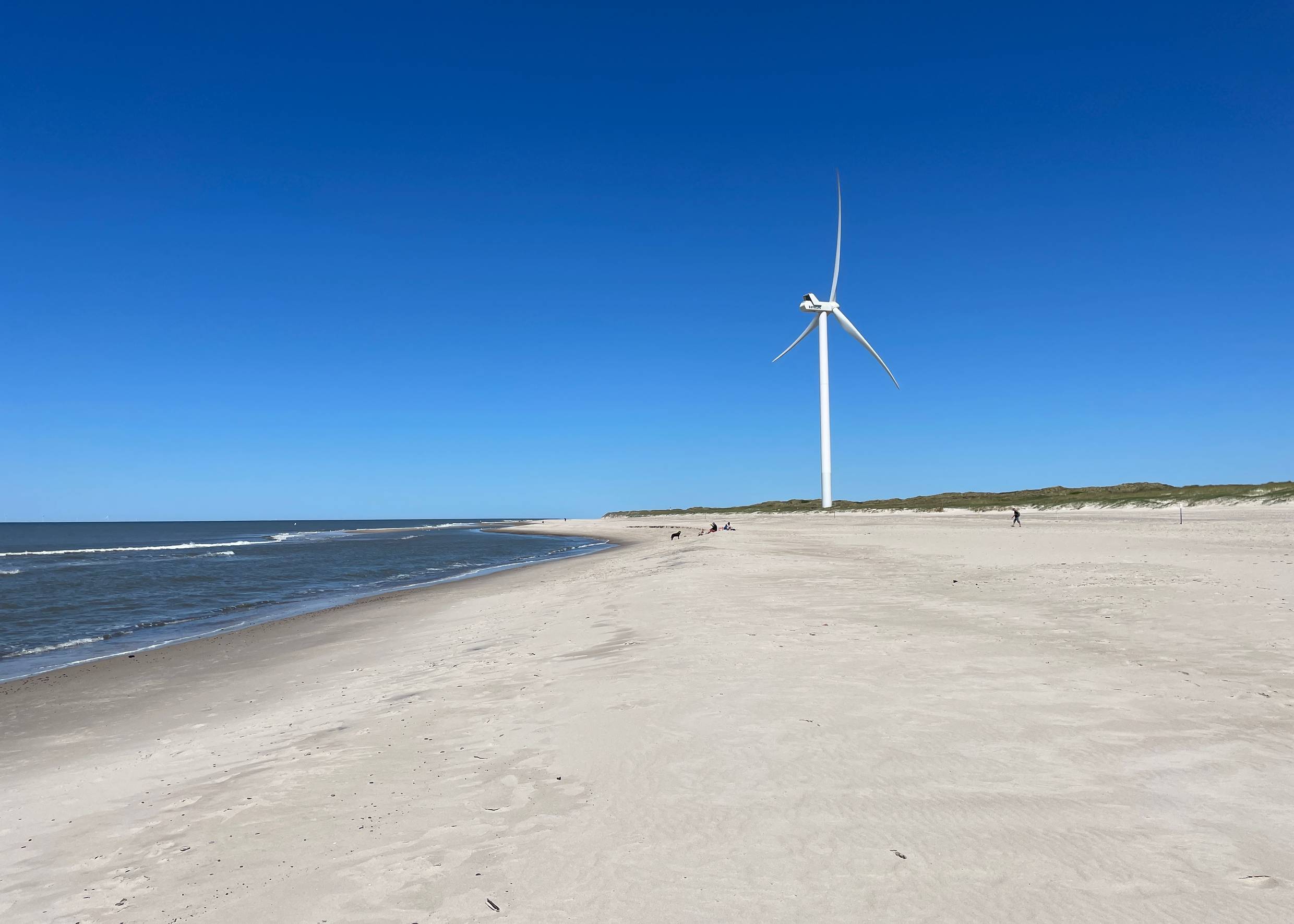 Nordseestrand mit Windrad unter weißen Wolken am blauen Himmel