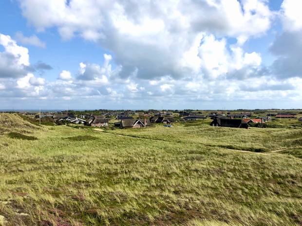 Blick von der Düne auf einen Siedlung mit großen Reetdachhäusern