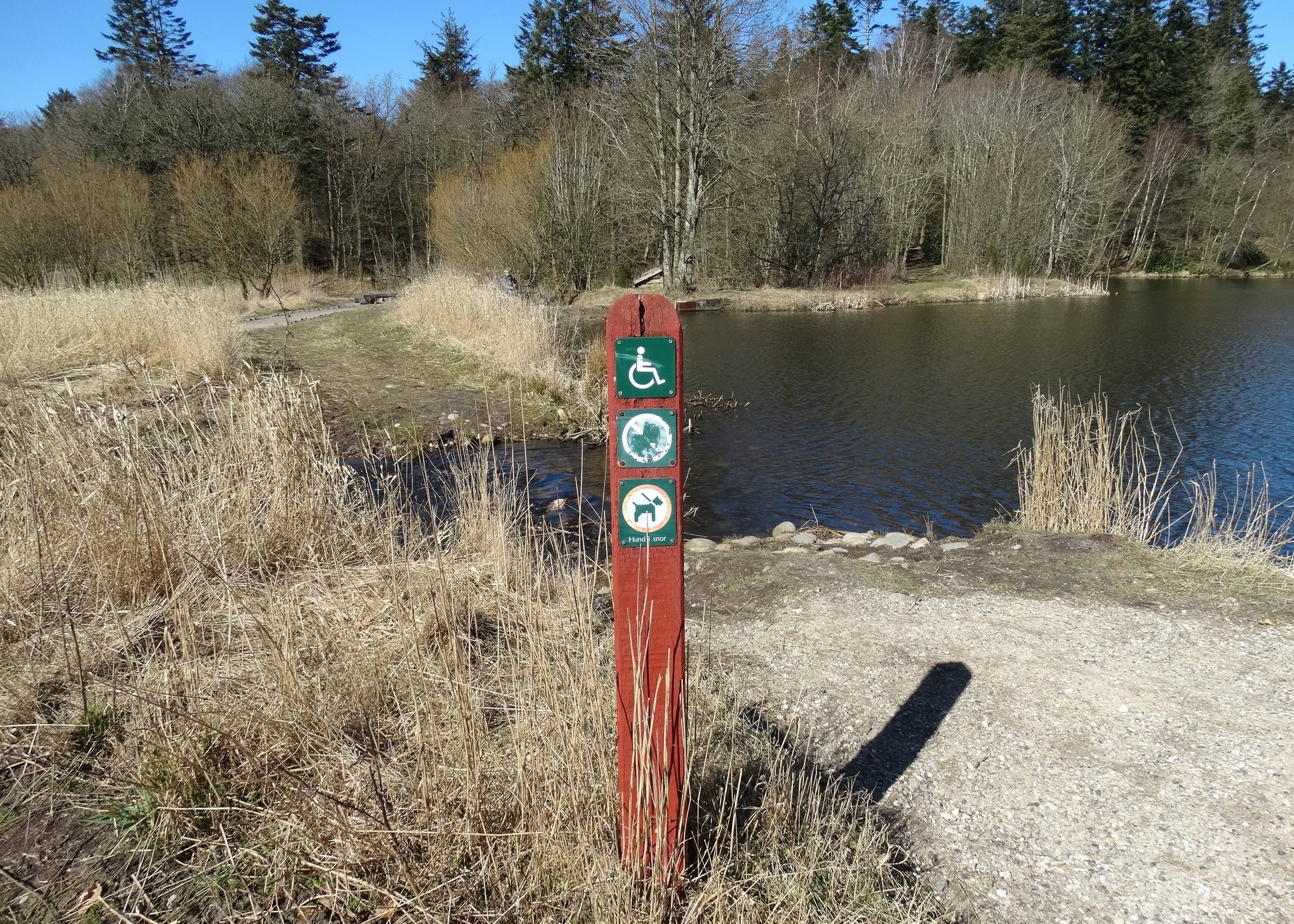 Roter Holzpfahl mit Hinweisschildern an einem See