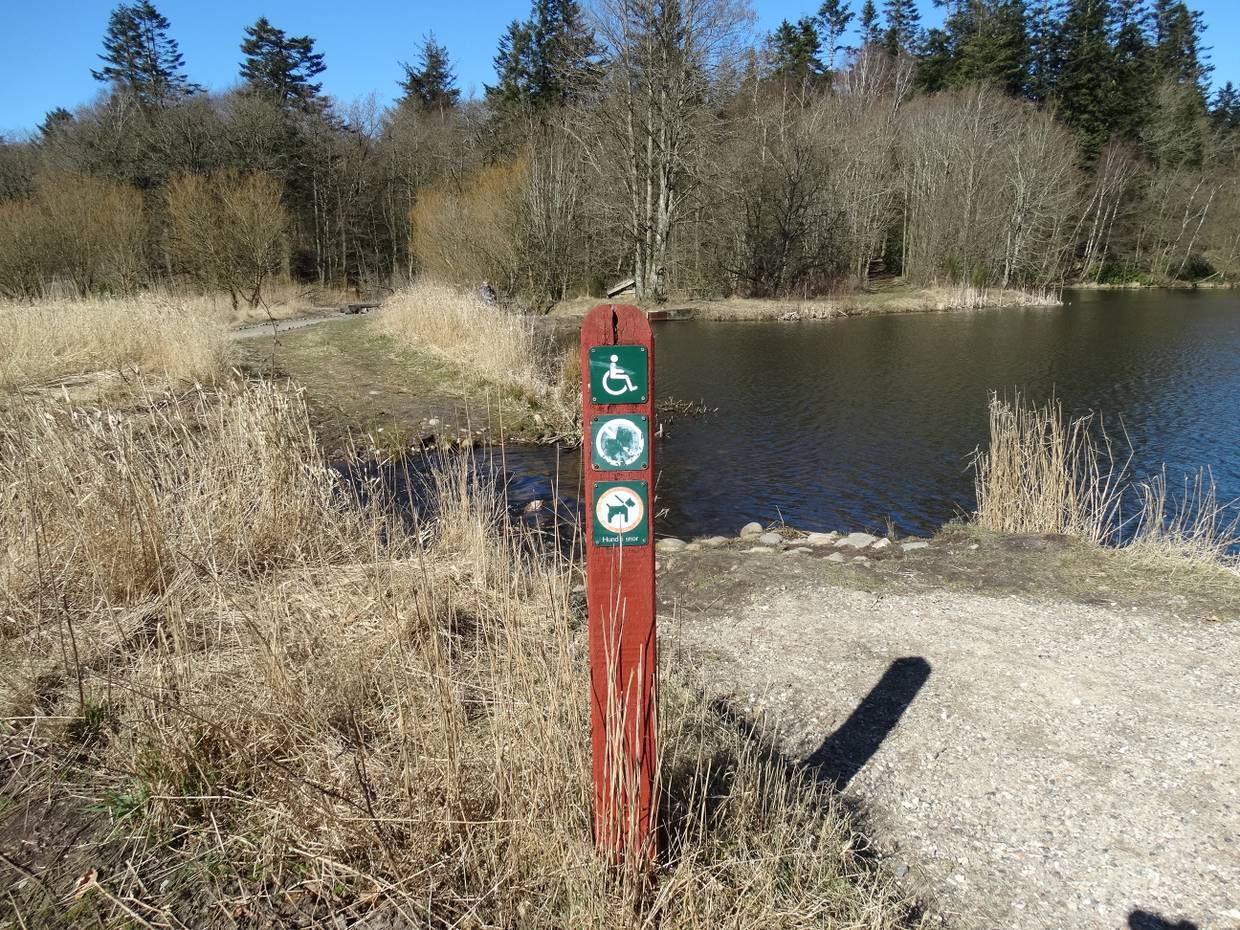 Roter Holzpfahl mit Hinweisschildern an einem See