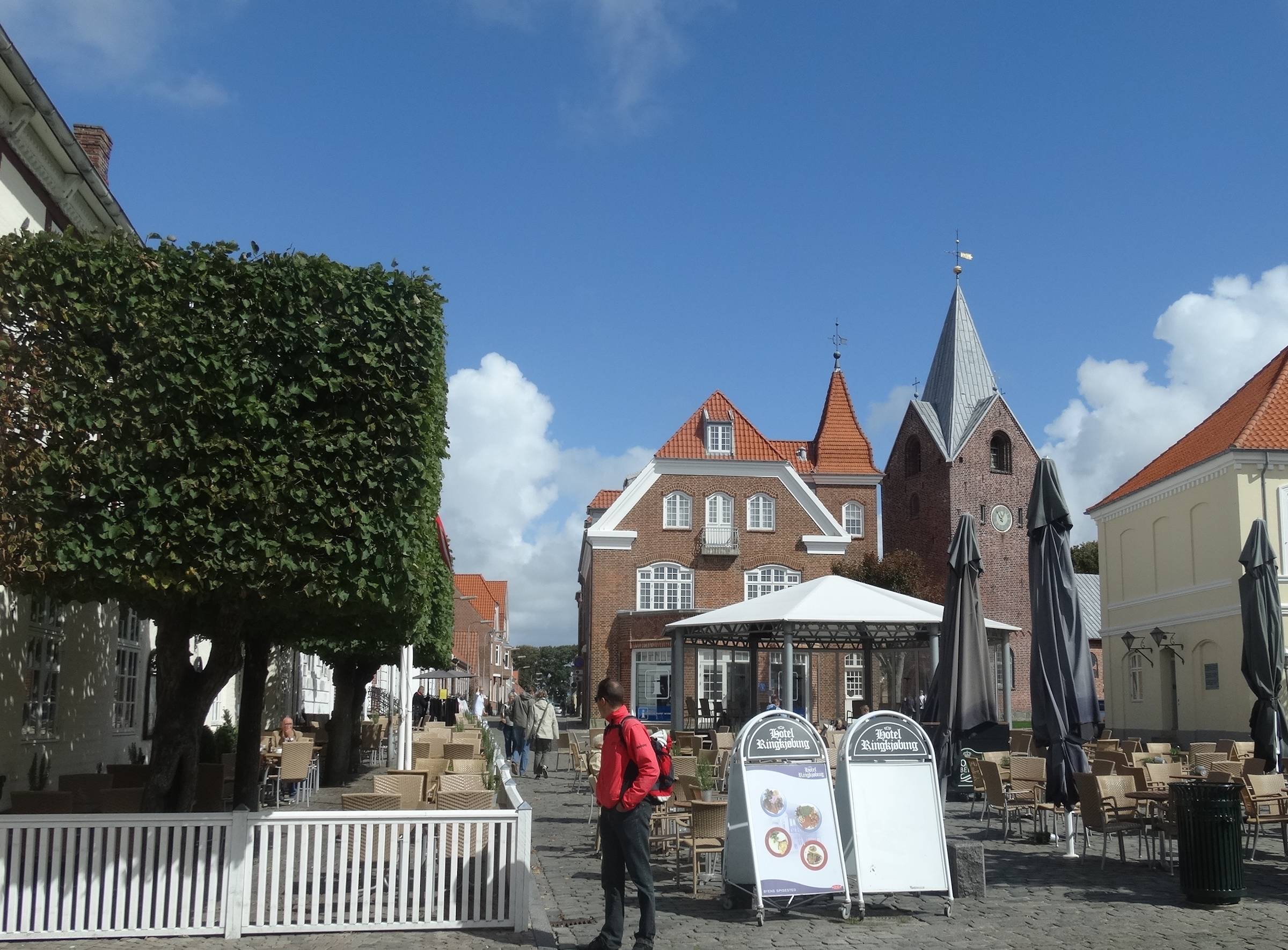 Kopfsteinpflasterplatz vor einer Kirche mit vielen Tischen eines Restaurants