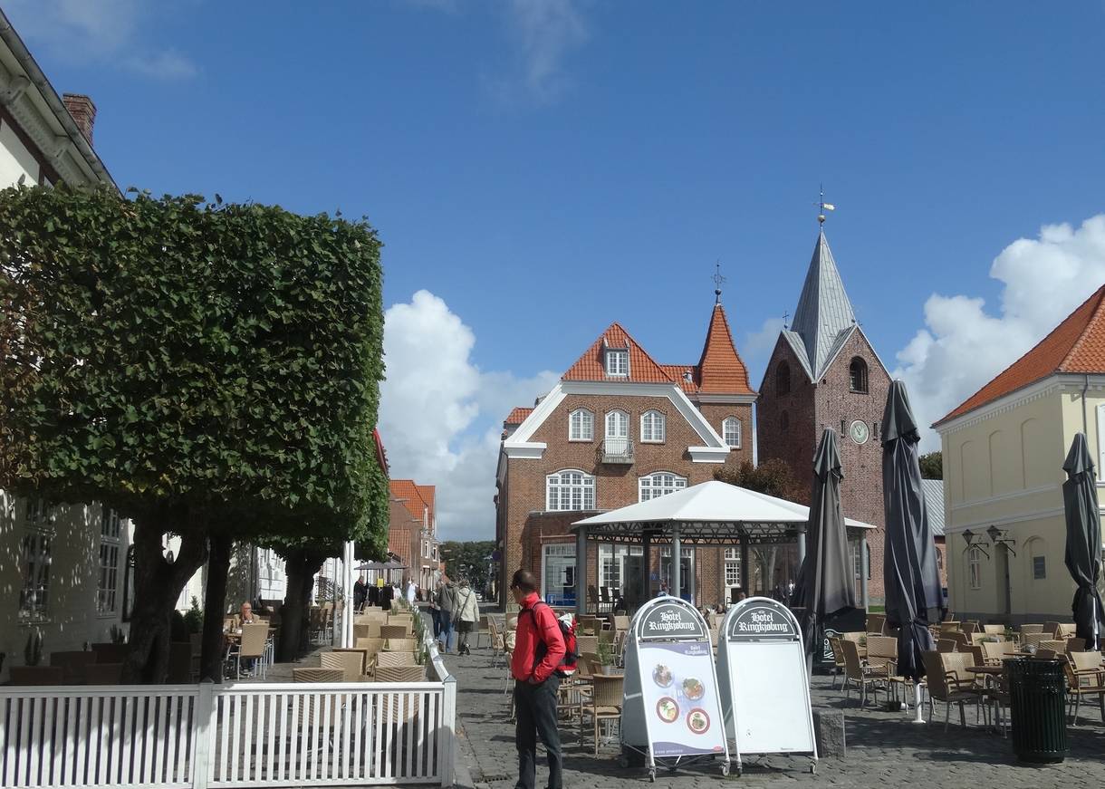Kopfsteinpflasterplatz vor einer Kirche mit vielen Tischen eines Restaurants