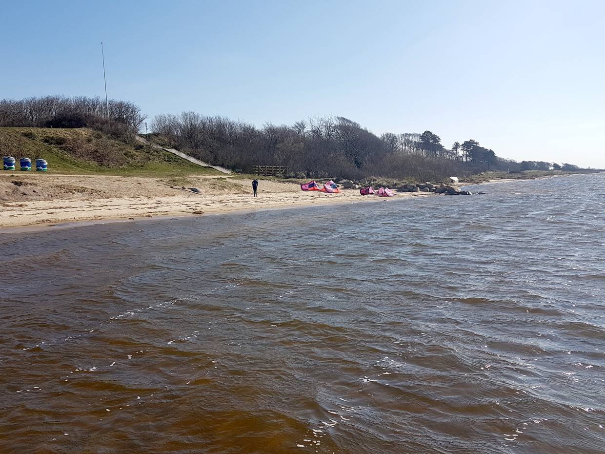 Blick auf einen schmalen Sandstrand am Fjord mit Kitezubehör