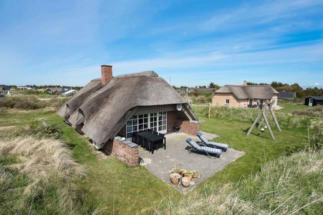 Reetdachferienhaus mit Liegestühlen und Spielgeräten im Garten