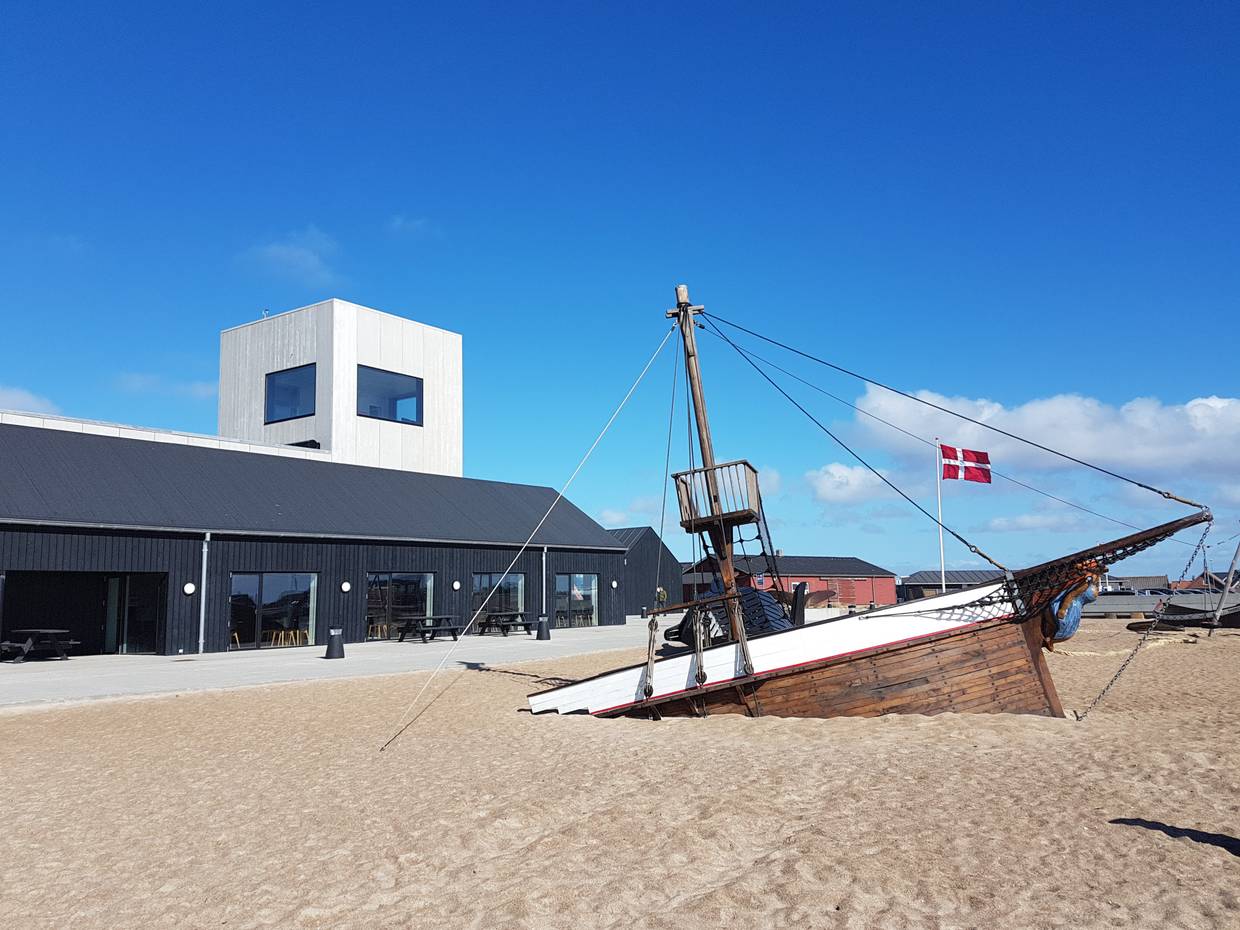 Versunkenes Schiff im Sand, dahinter ein modernes Museumsgebäude