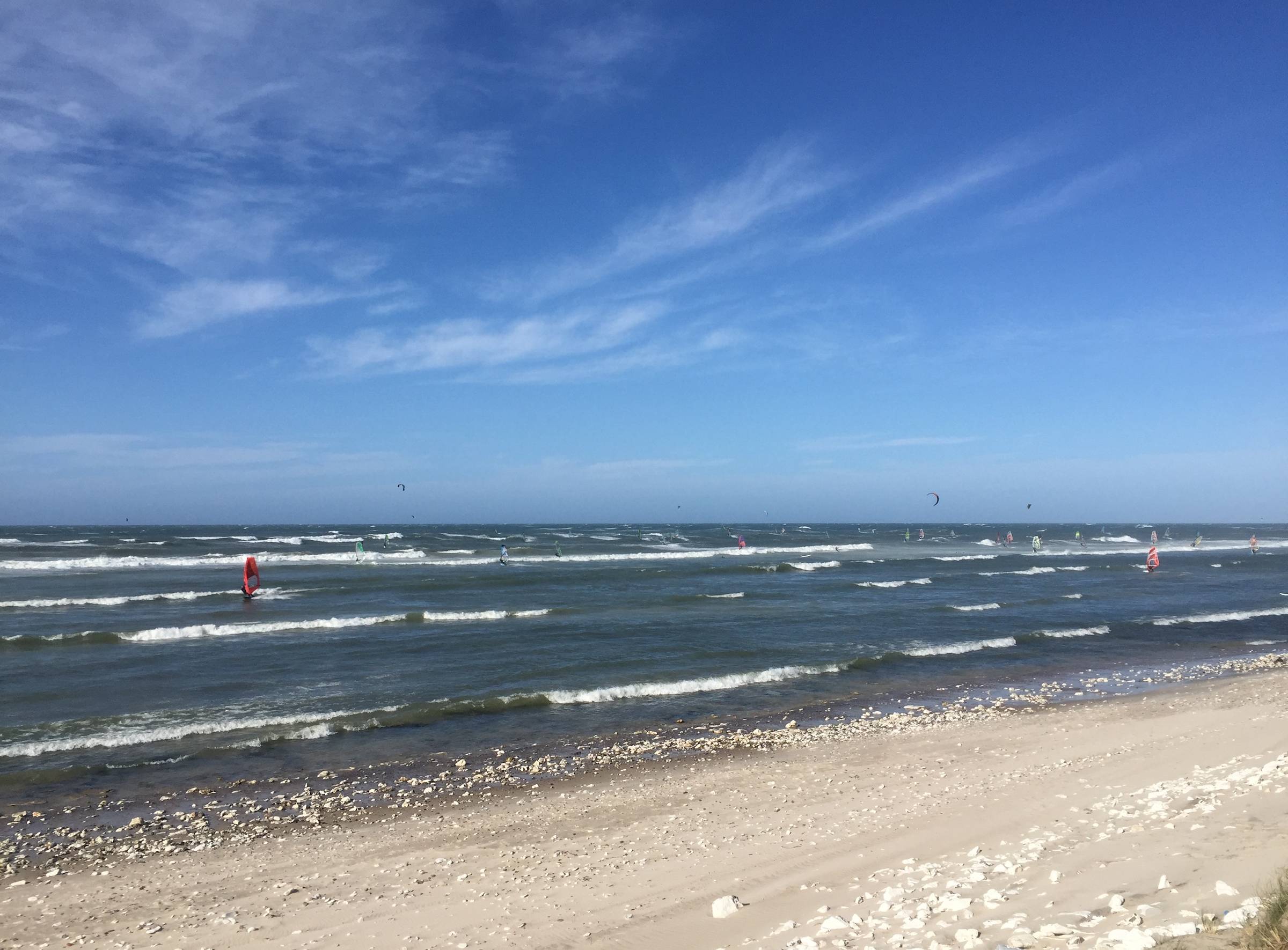 Flache Nordseewellen bei Sonne mit Surfern und Kitern