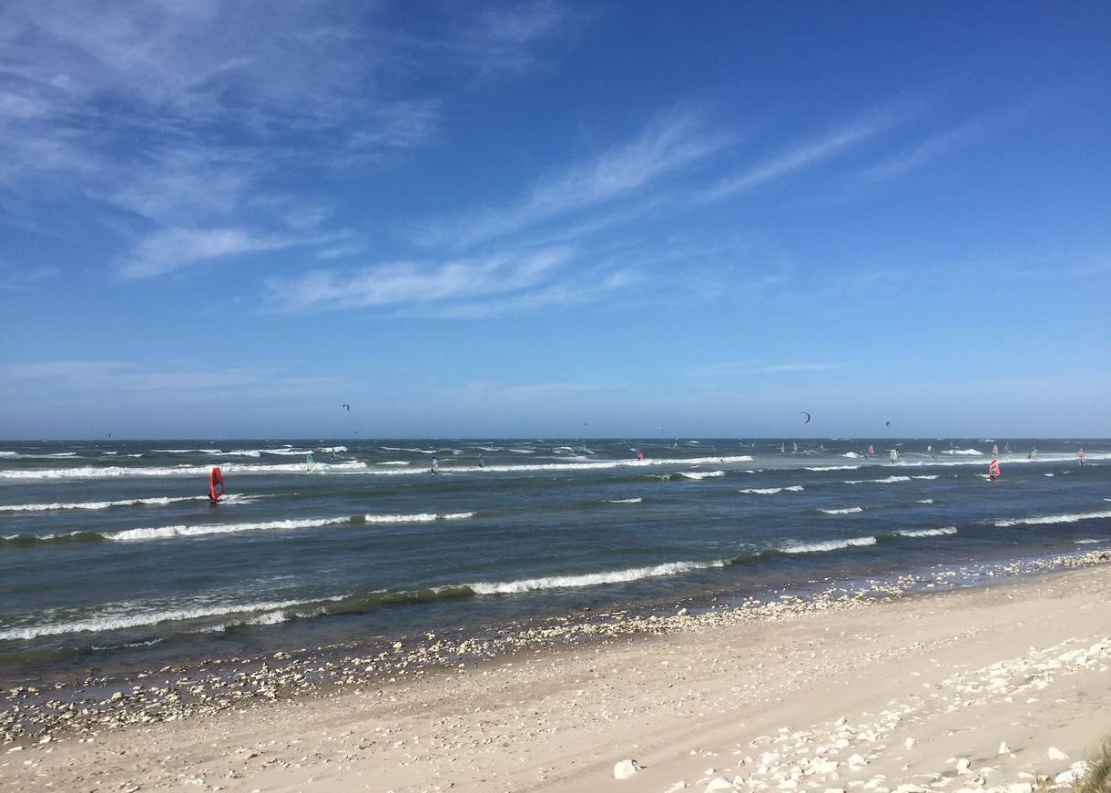 Flache Nordseewellen bei Sonne mit Surfern und Kitern