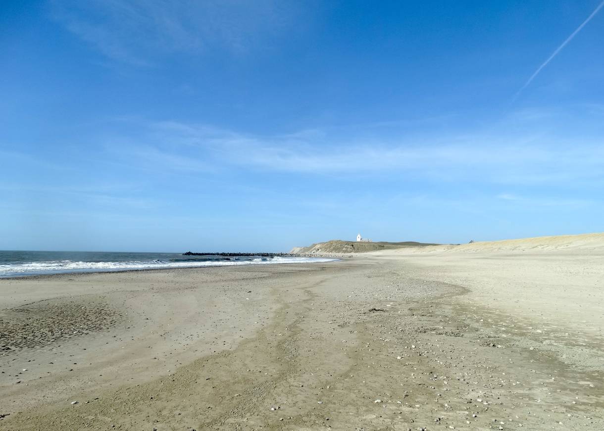 Blick über einen langen Strand, im Hintergrund eine Kirche auf den Dünen