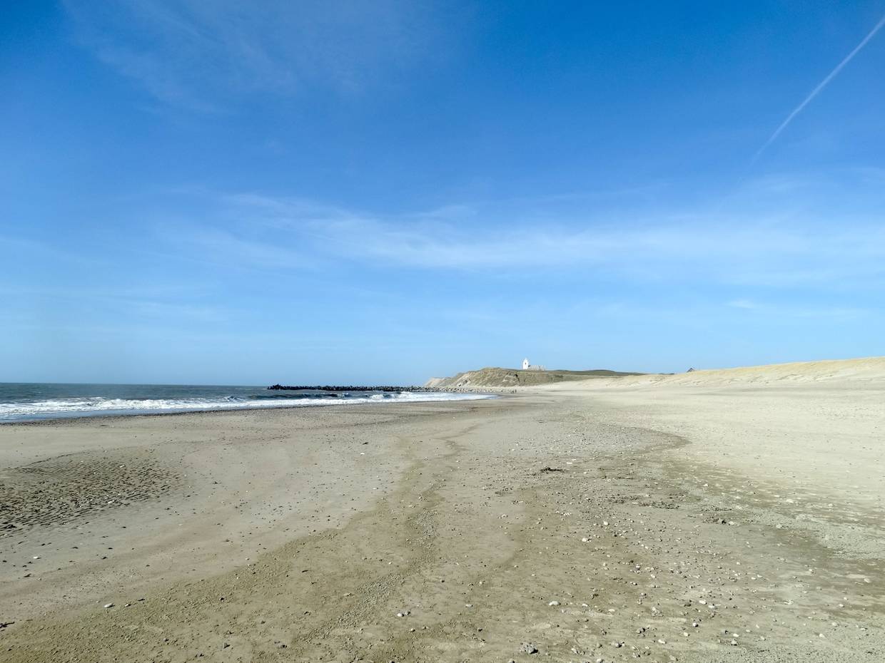 Blick über einen langen Strand, im Hintergrund eine Kirche auf den Dünen