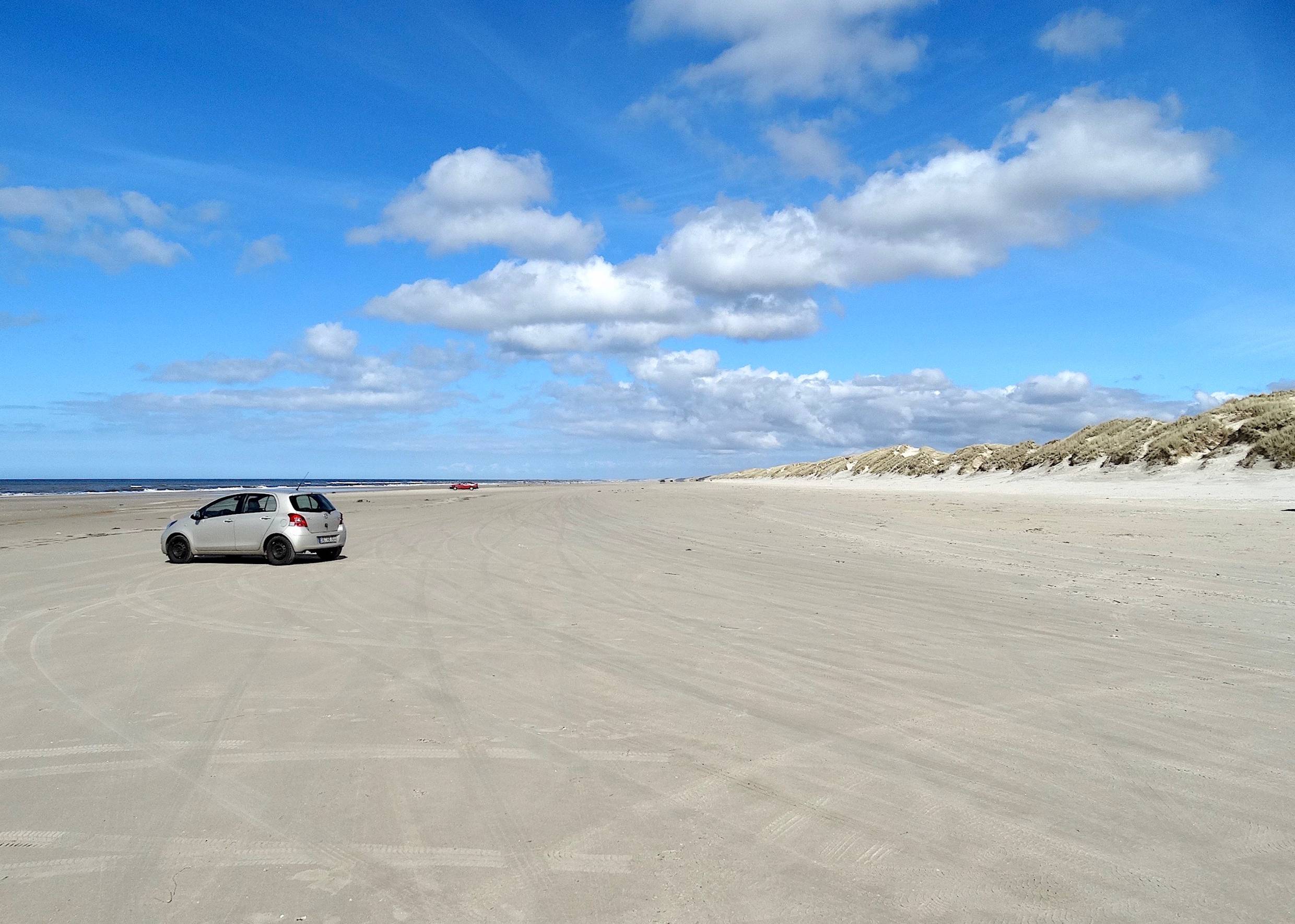 Breiter, weißer Sandstrand mit einem Auto