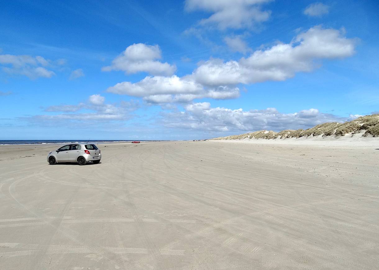 Breiter, weißer Sandstrand mit einem Auto
