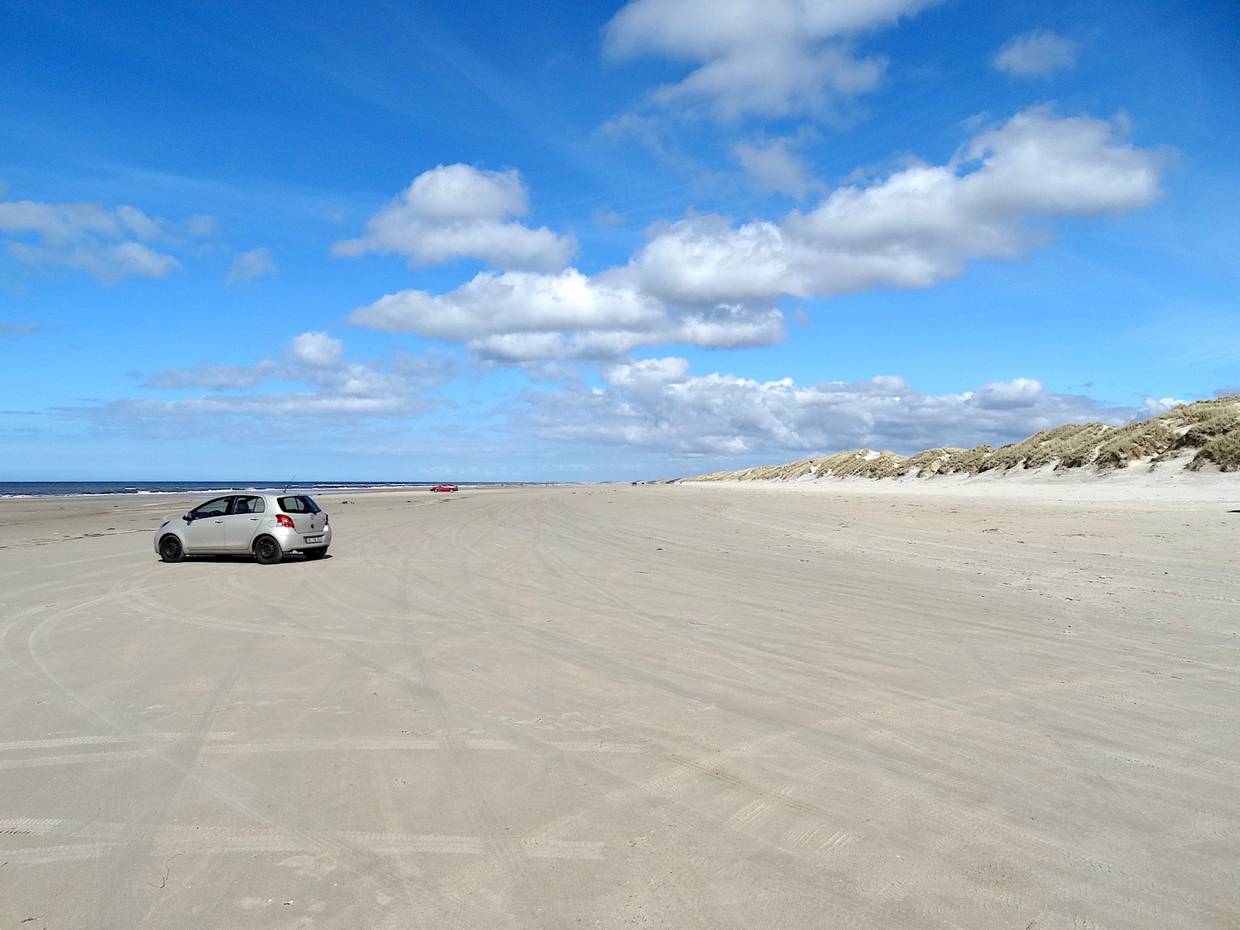 Breiter, weißer Sandstrand mit einem Auto
