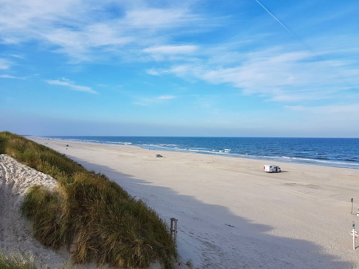 Breiter Sandstrand mit Autos in der Ferne