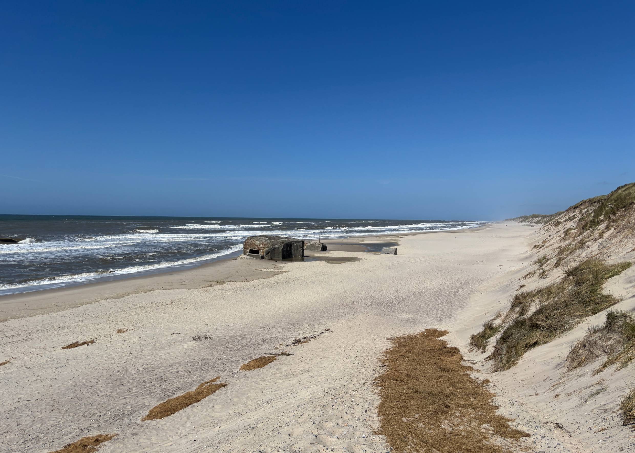 Blick über einen breiten Strand mit Dünen und einem Bunker 