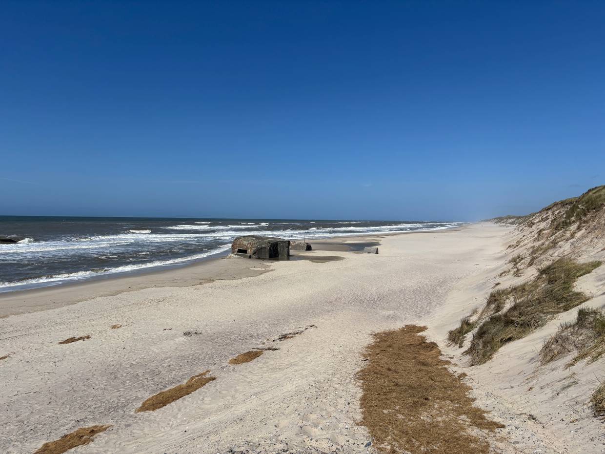 Blick über einen breiten Strand mit Dünen und einem Bunker 