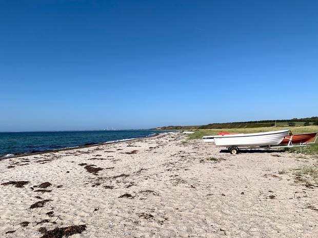 Eine Bucht mit einer schmalen Sandstrand im Vordergrund kleine Boote auf Land