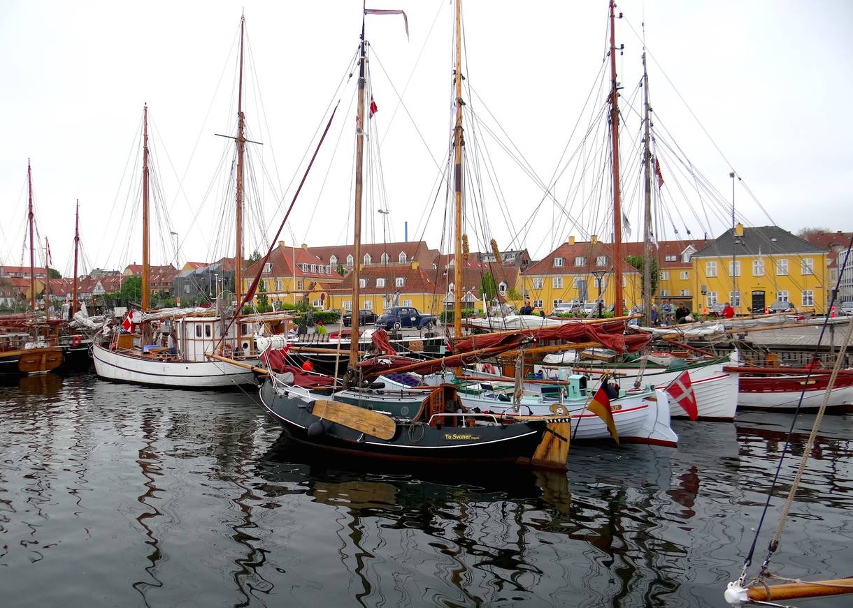 Alte Holzsegelschiffe im Hafen, dahinter gelbe Häuser