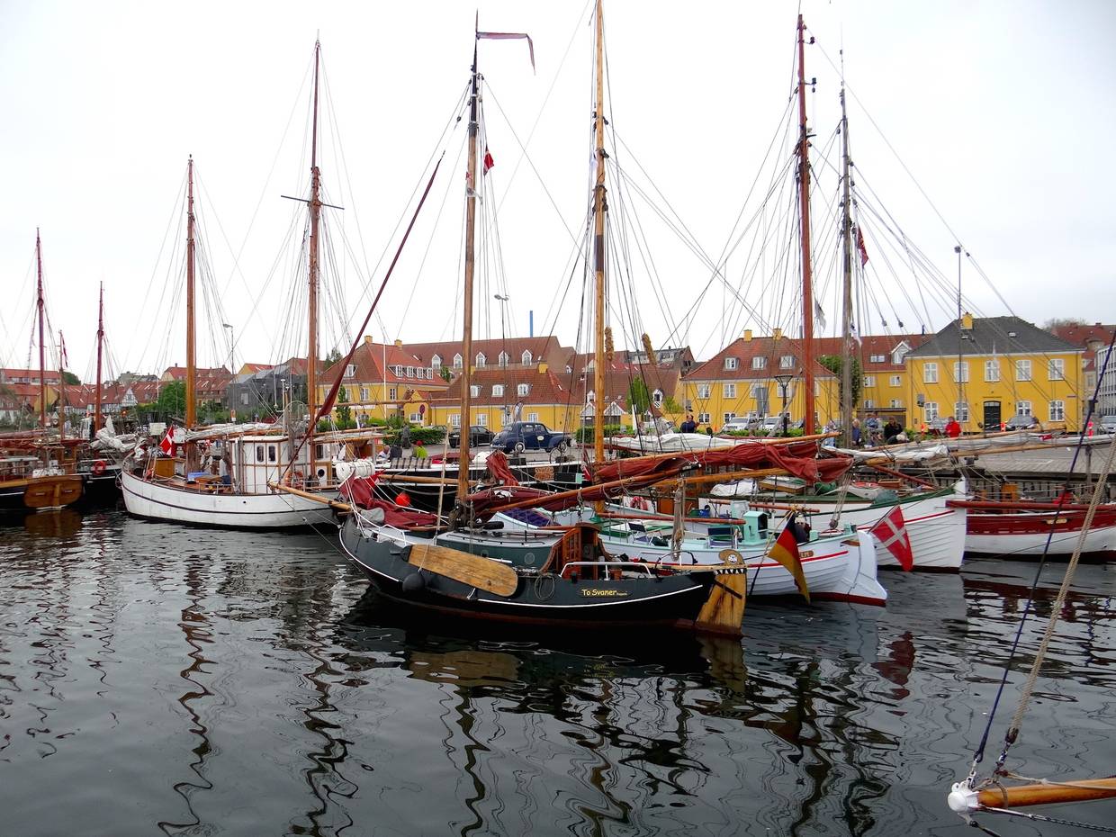 Alte Holzsegelschiffe im Hafen, dahinter gelbe Häuser